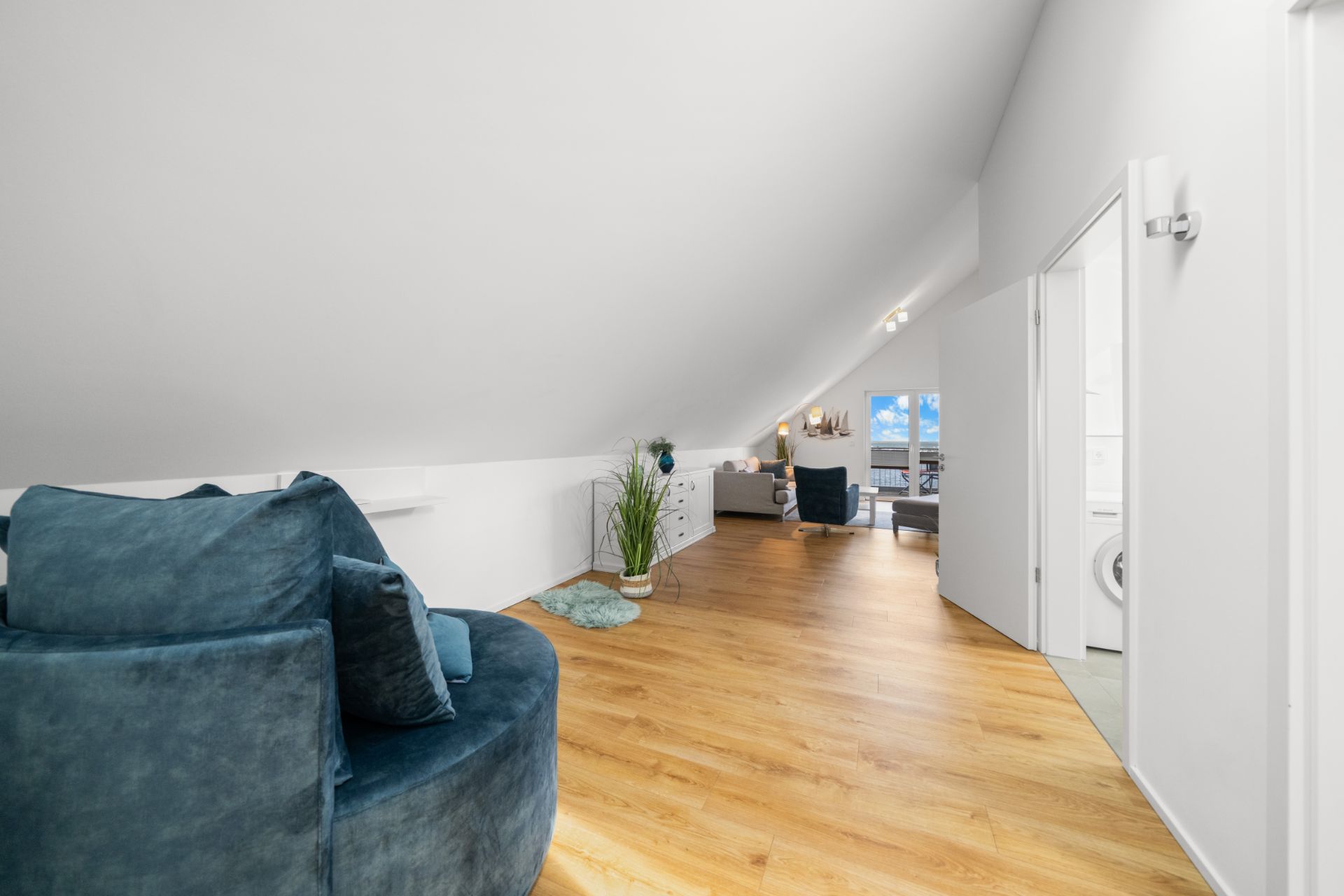 Heller Dachgeschossraum mit Holzfußboden, Sitzmöbel, Kommode und Pflanzen.