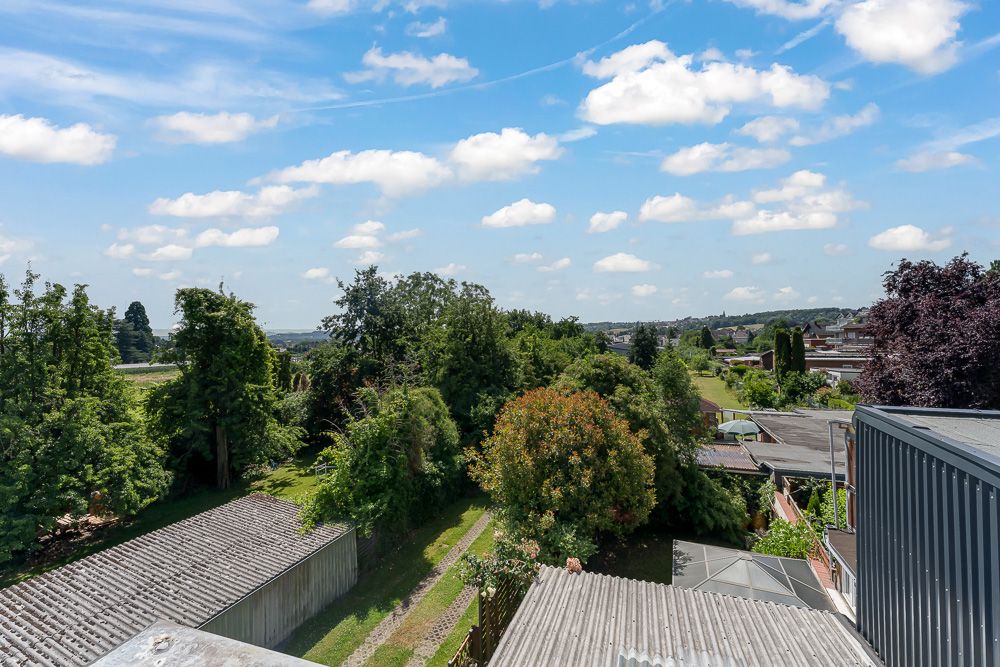 Blick über einen Garten mit Bäumen, Nebengebäuden und weitem Himmel.