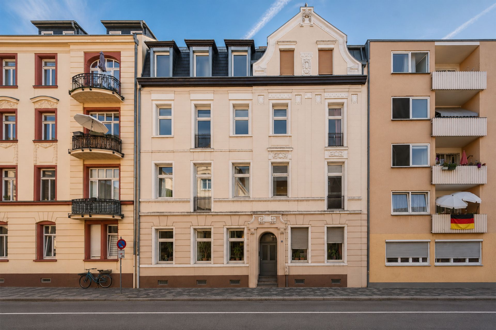 Fassade eines mehrstöckigen Wohnhauses mit mehreren Fenstern und Haustür, flankiert von Nachbargebäuden.