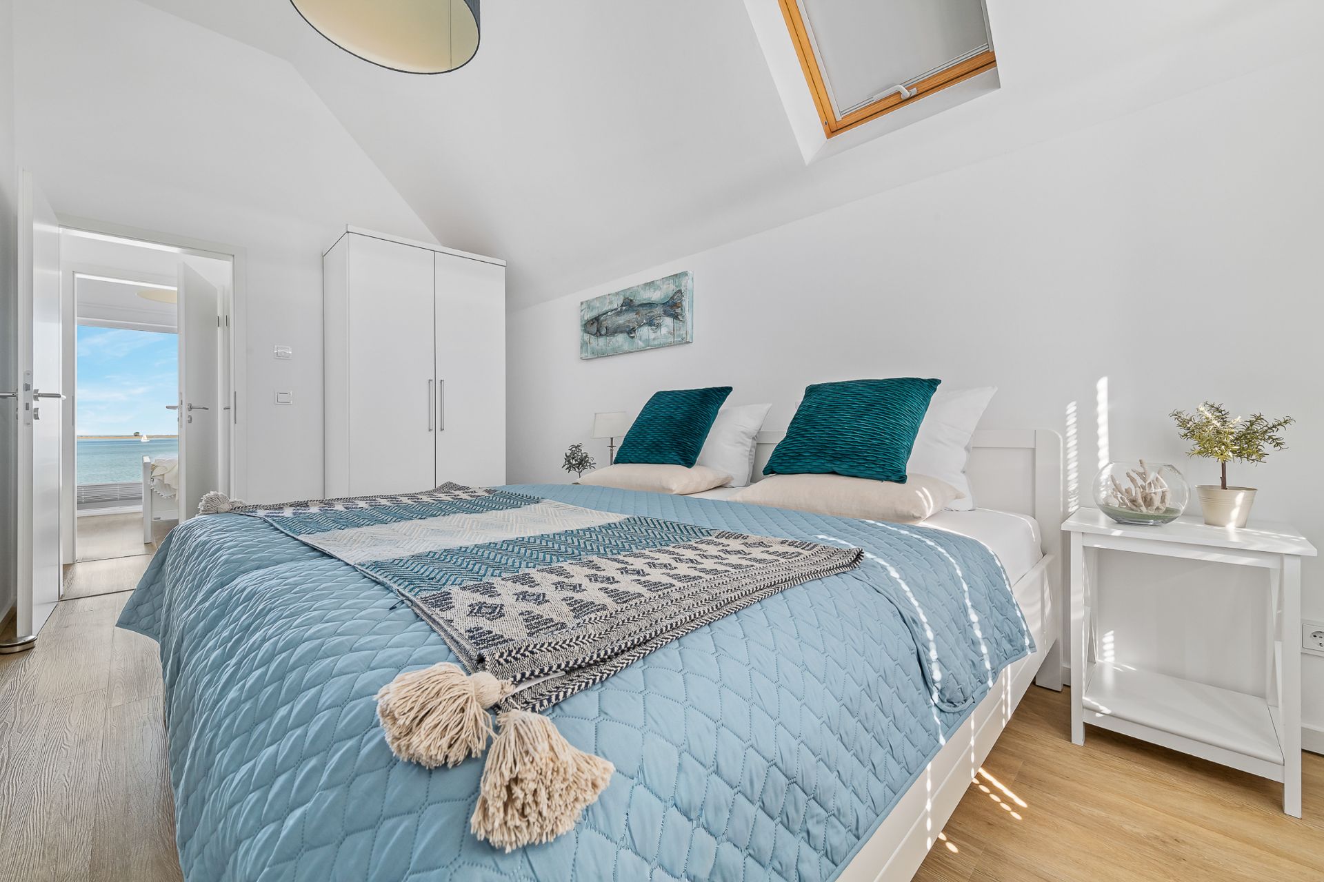 Helles Schlafzimmer mit Doppelbett, weißem Schrank, Nachttisch und Fenster im Dach.