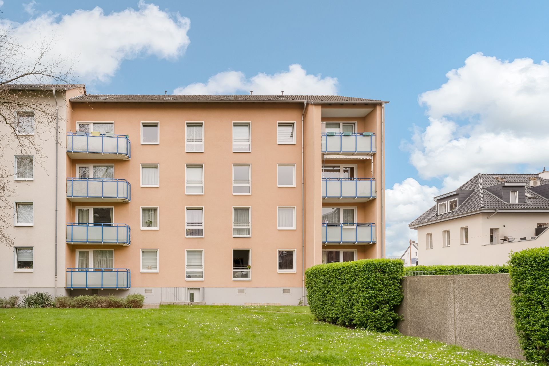 Mehrfamilienhaus mit mehreren Balkonen und gepflegtem grünen Garten davor.