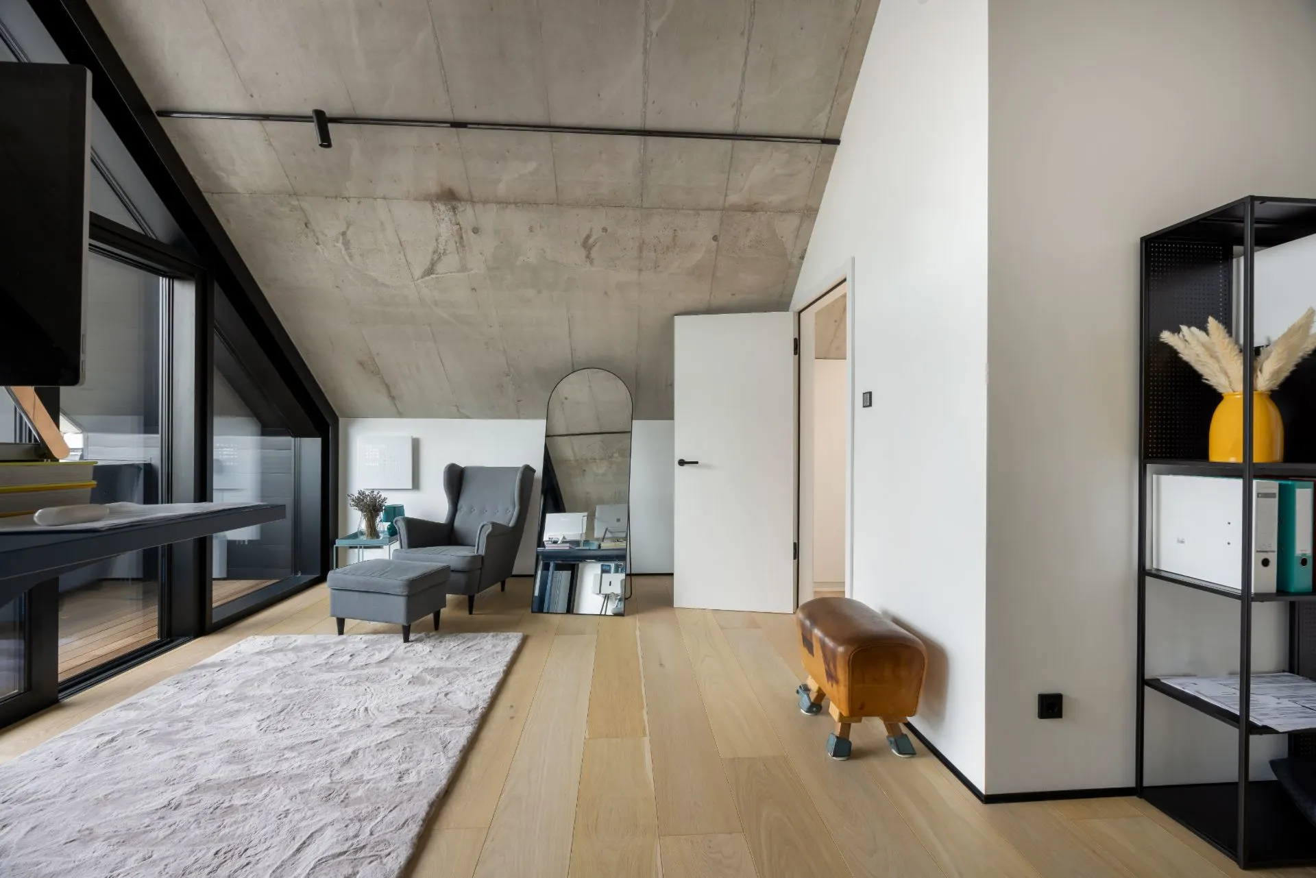Modernes Zimmer mit schrägem Dach, Sessel, Teppich, Regal und großem Fenster.