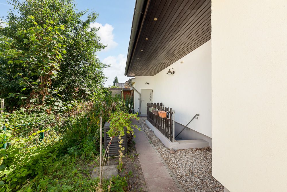 Seitlicher Eingang eines Hauses mit Kiesweg, Zaun und grünem Garten.
