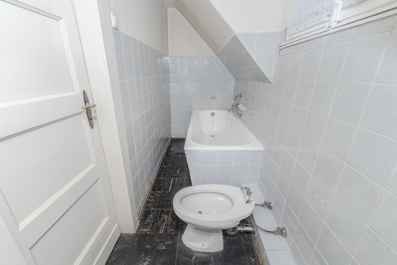 Kleines Badezimmer mit Badewanne und Bidet, blaue Fliesen an Wand und schwarzer Boden.