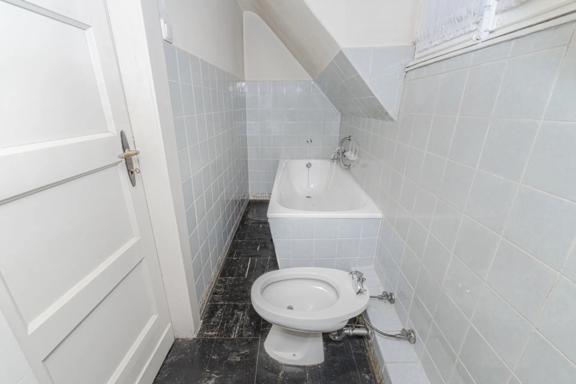 Kleines Badezimmer mit Badewanne und Bidet, blaue Fliesen an Wand und schwarzer Boden.