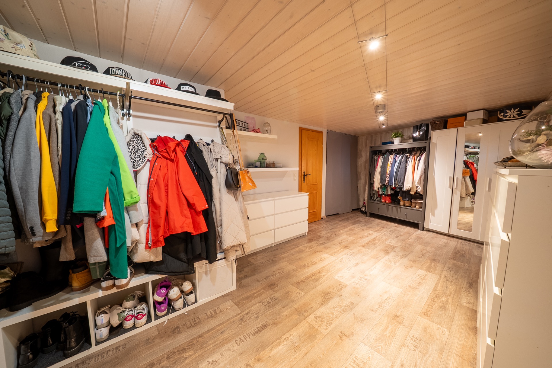 Großer begehbarer Kleiderschrank mit Kleidung, Schuhen, Regalen und Kommoden auf Holzfußboden.