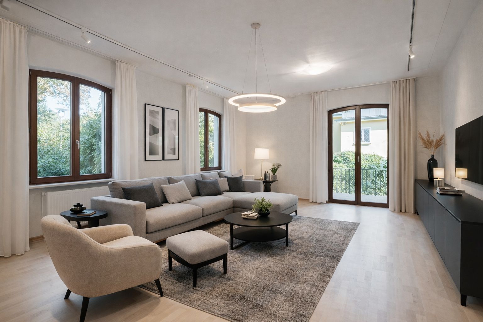 Helles Wohnzimmer mit Sofa, Sessel, Couchtisch, Teppich, TV und großen Fenstern mit Blick ins Grüne.
