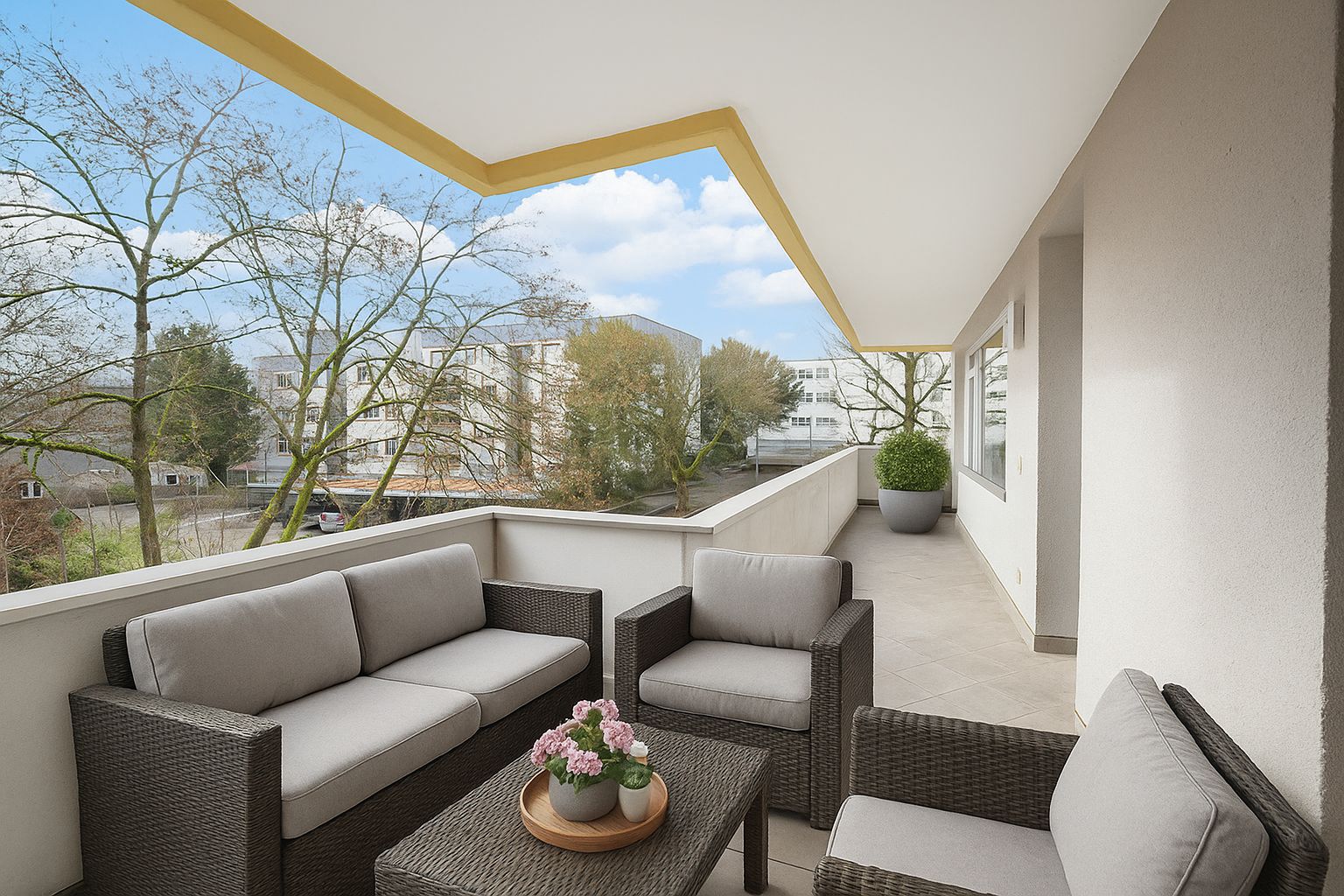 Großer Balkon mit Sitzgruppe, Tisch und Topfpflanzen, Blick auf Bäume und Wohnhäuser.