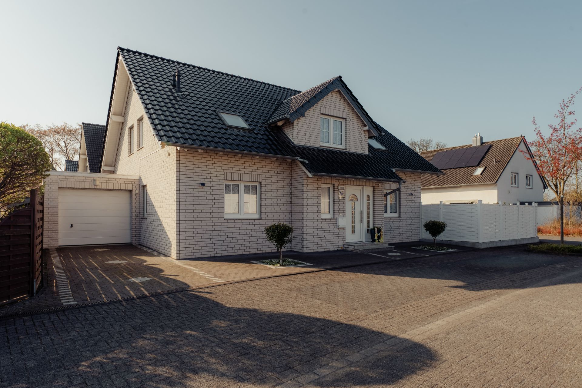 Modernes Einfamilienhaus mit dunklem Dach, Garage und Vorgarten, aufgenommen bei Tageslicht.