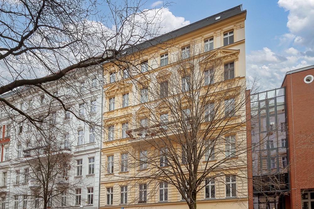 Mehrstöckiges Wohngebäude mit gelber Fassade und Balkonen, davor kahle Bäume.
