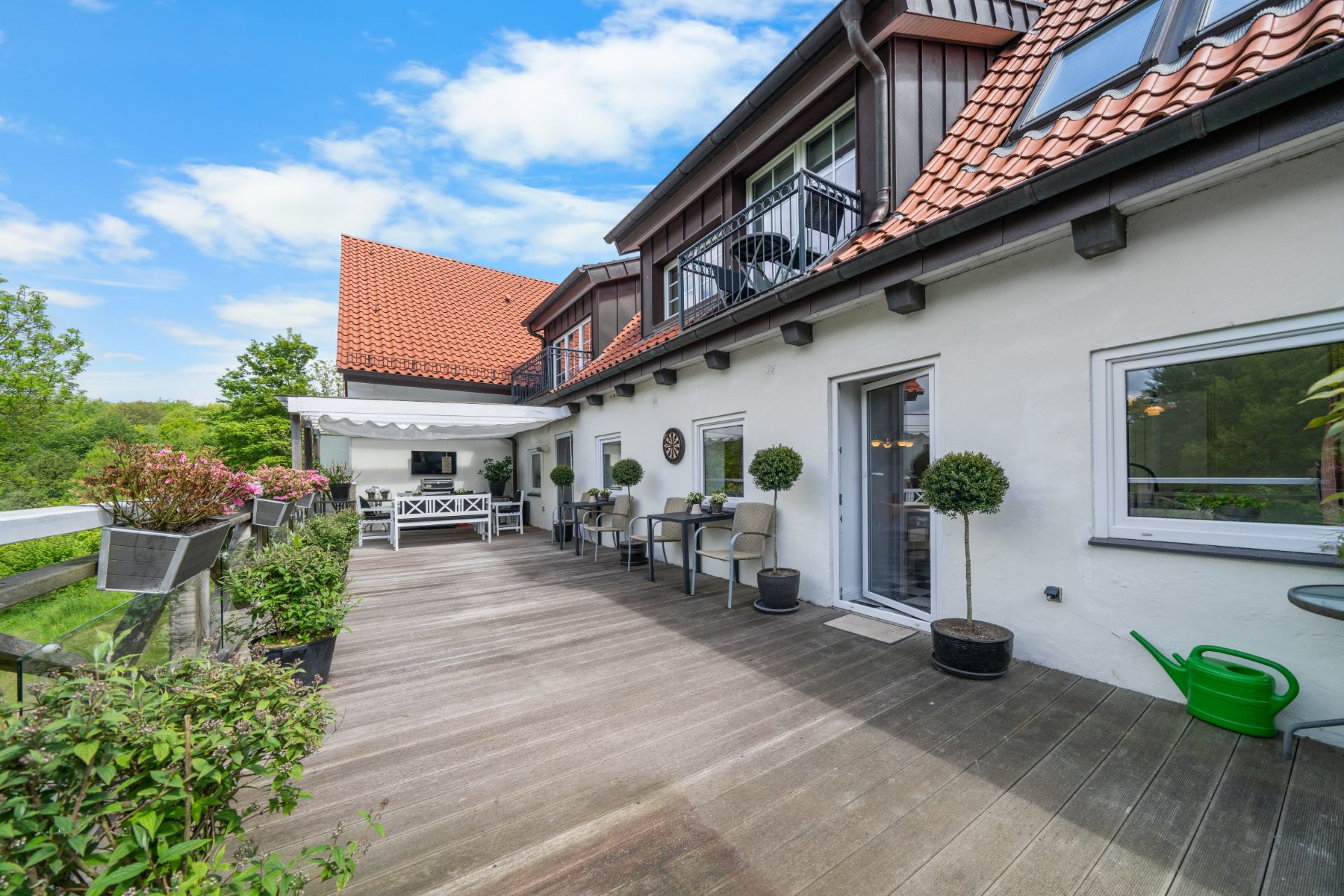Große Terrasse mit Holzboden, Pflanzen und Gartenmöbeln an einem Wohnhaus.