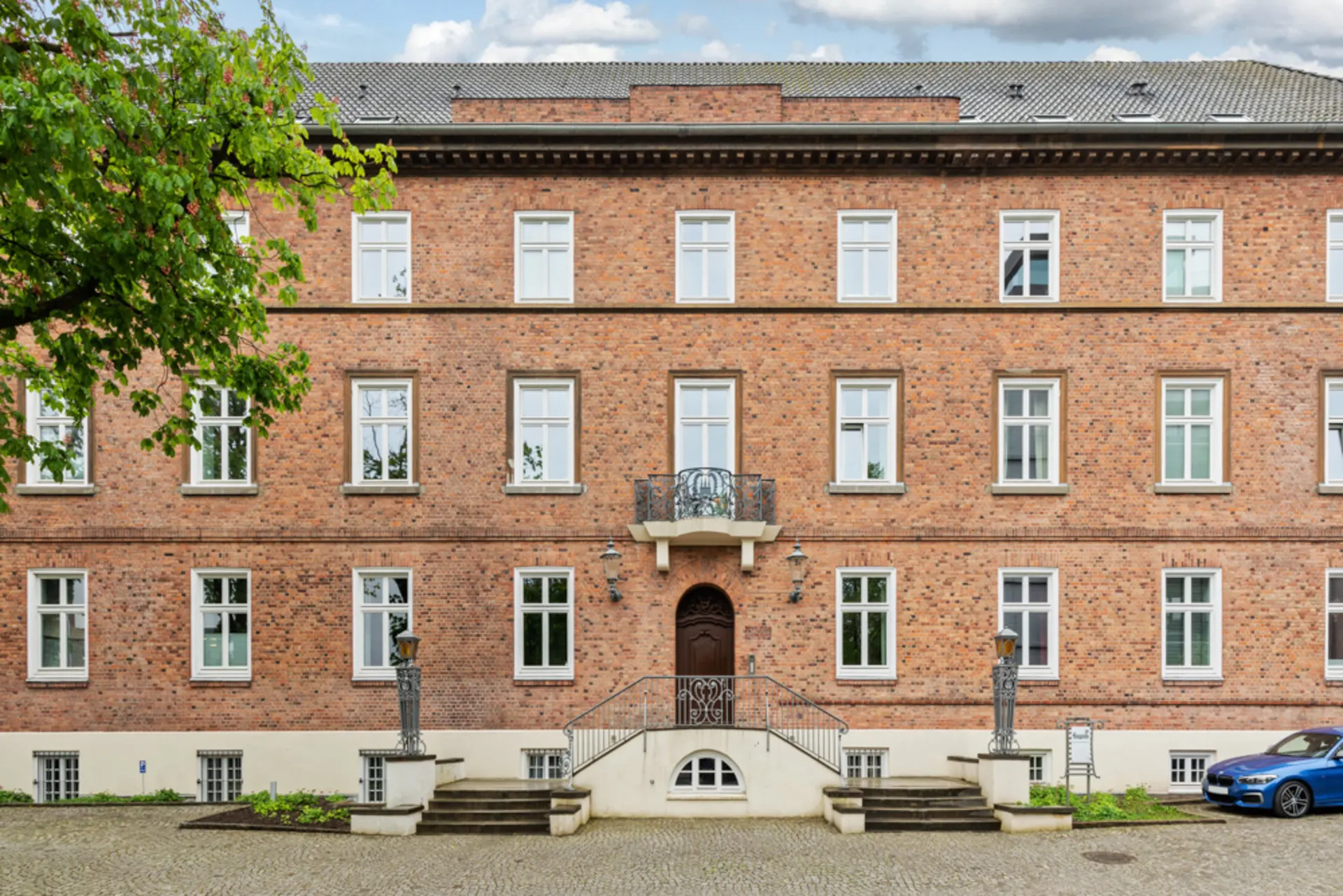 Dreistöckiges Backsteingebäude mit vielen weißen Fenstern und einer zentralen Eingangstreppe.