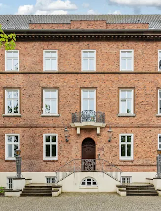 Dreistöckiges Backsteingebäude mit vielen weißen Fenstern und einer zentralen Eingangstreppe.