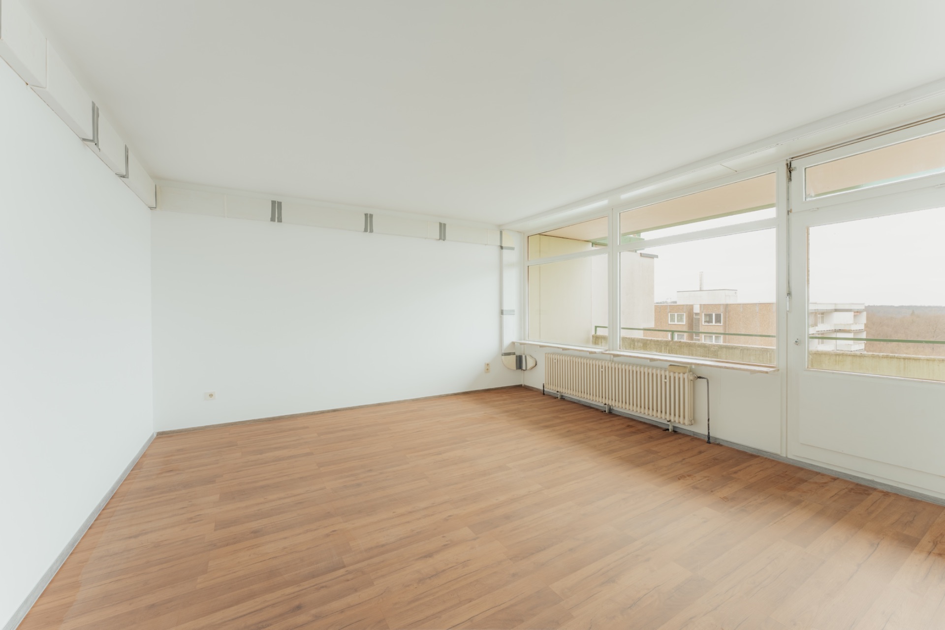Helles, leeres Zimmer mit Holzfußboden und großen Fenstern sowie Zugang zum Balkon.