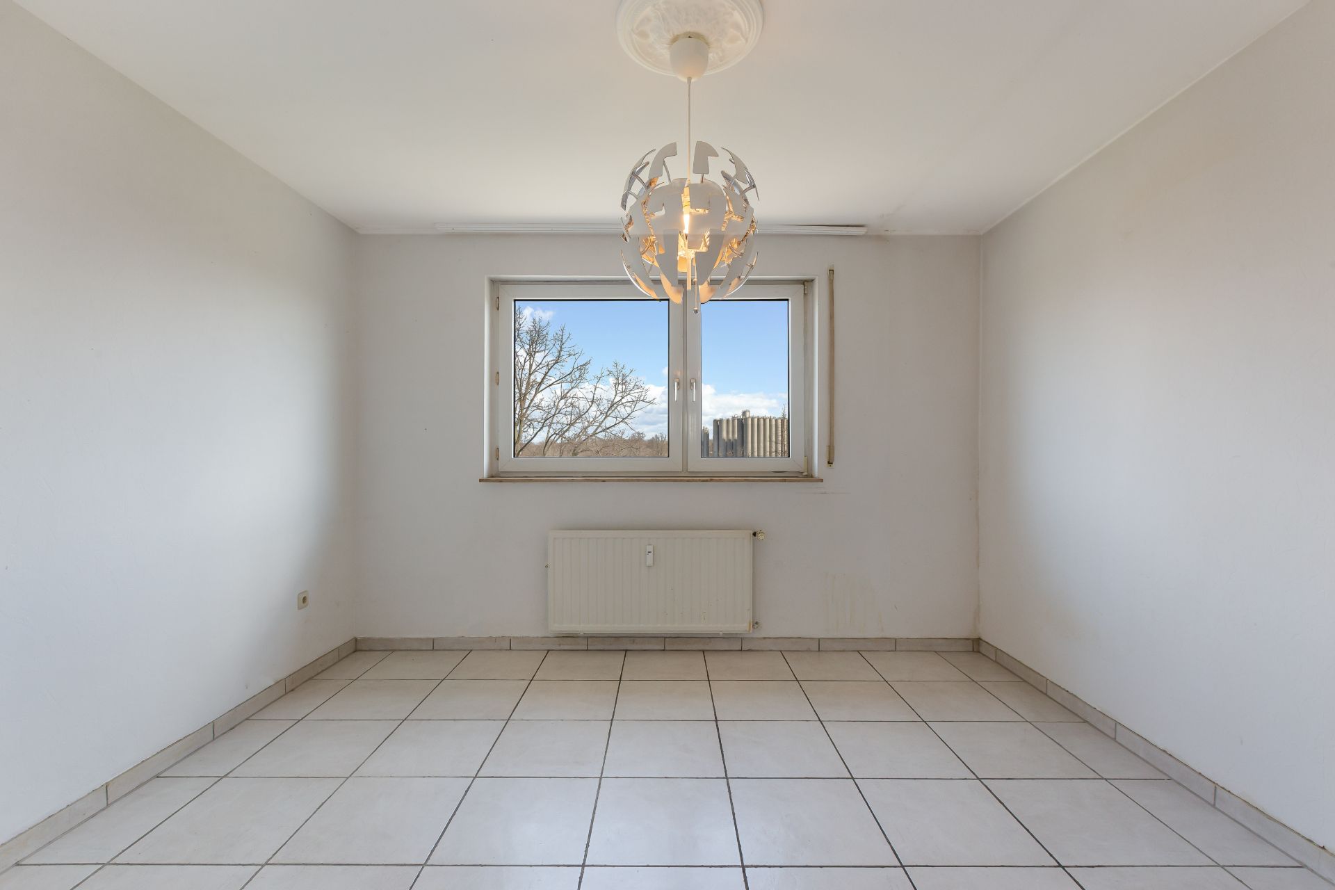 Leerer Raum mit weißen Wänden, Fliesenboden, Fenster und moderner Deckenleuchte.