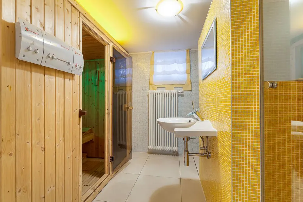 Helles Badezimmer mit Sauna, Waschbecken, gelben Fliesen und Fenster mit Vorhang.