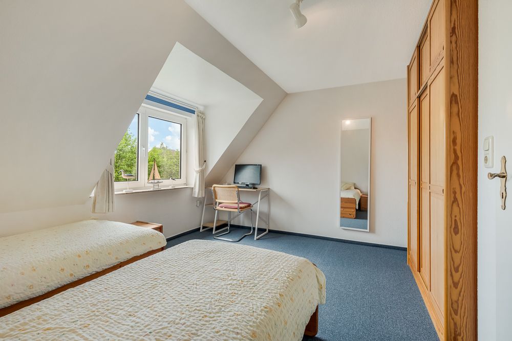 Helles Schlafzimmer mit zwei Einzelbetten, Schrank, Schreibtisch, Stuhl und Fenster.