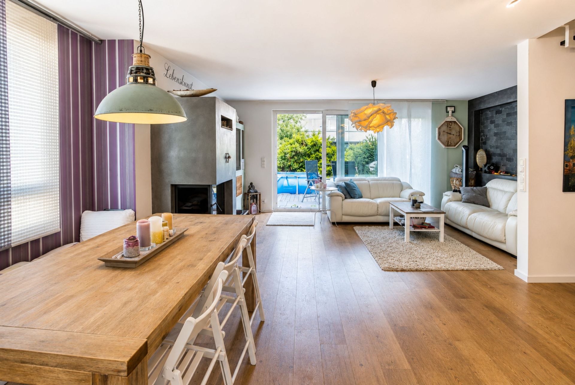 Helles Wohnzimmer mit Holzboden, Esstisch, weißen Sofas und Blick auf den Garten.