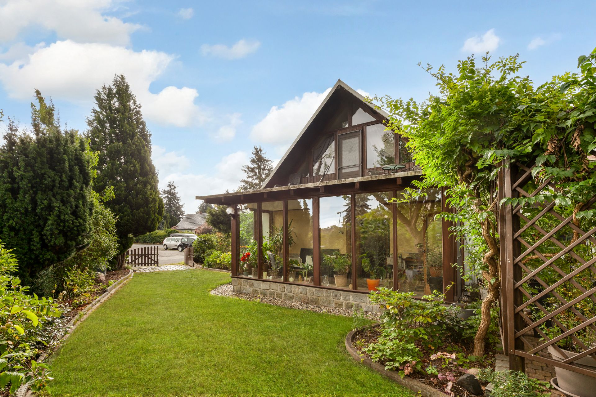 Garten mit Rasen und Blick auf ein Haus mit Wintergarten und viel Glas.