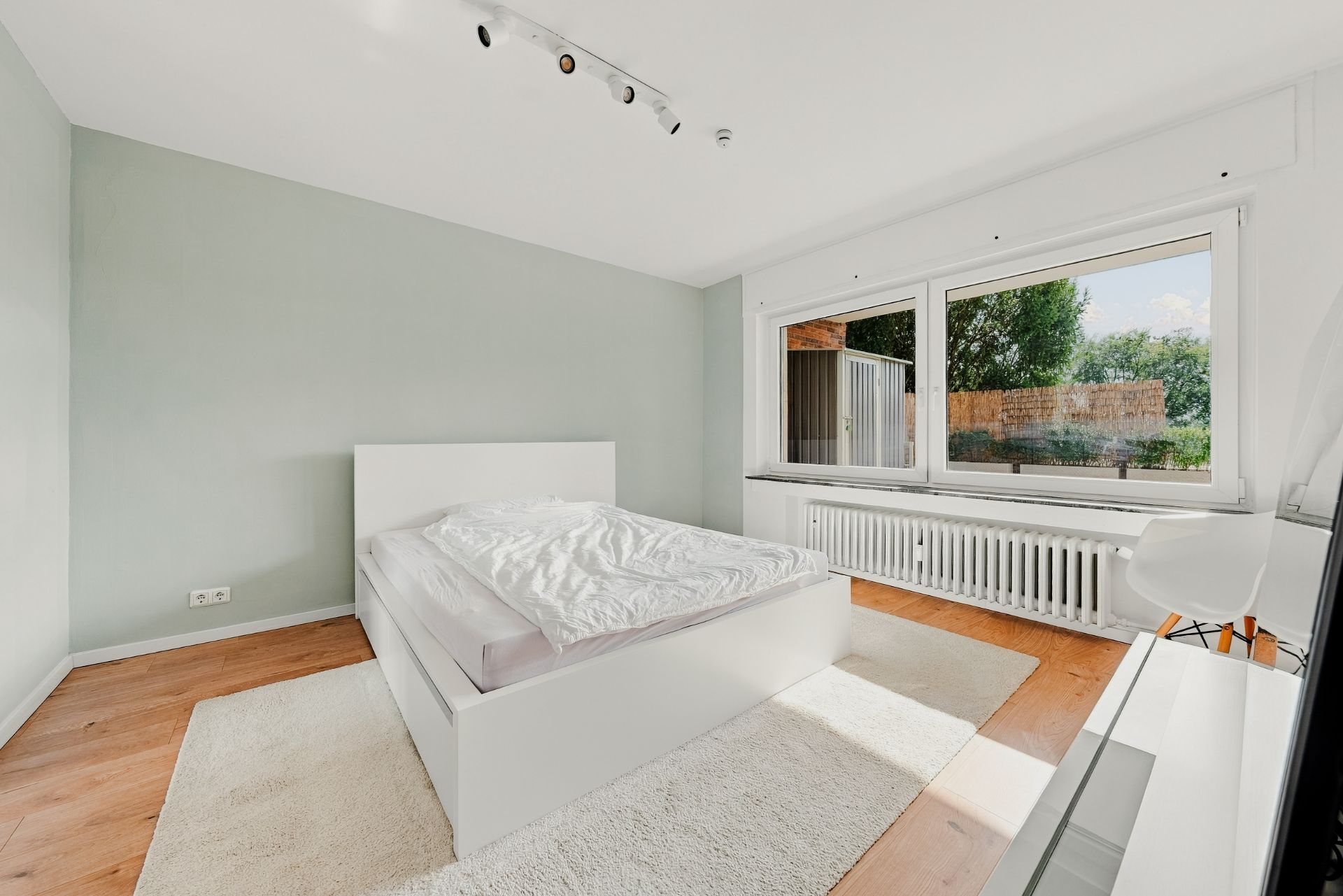 Helles Schlafzimmer mit großem Fenster, weißem Bett und Holzboden.