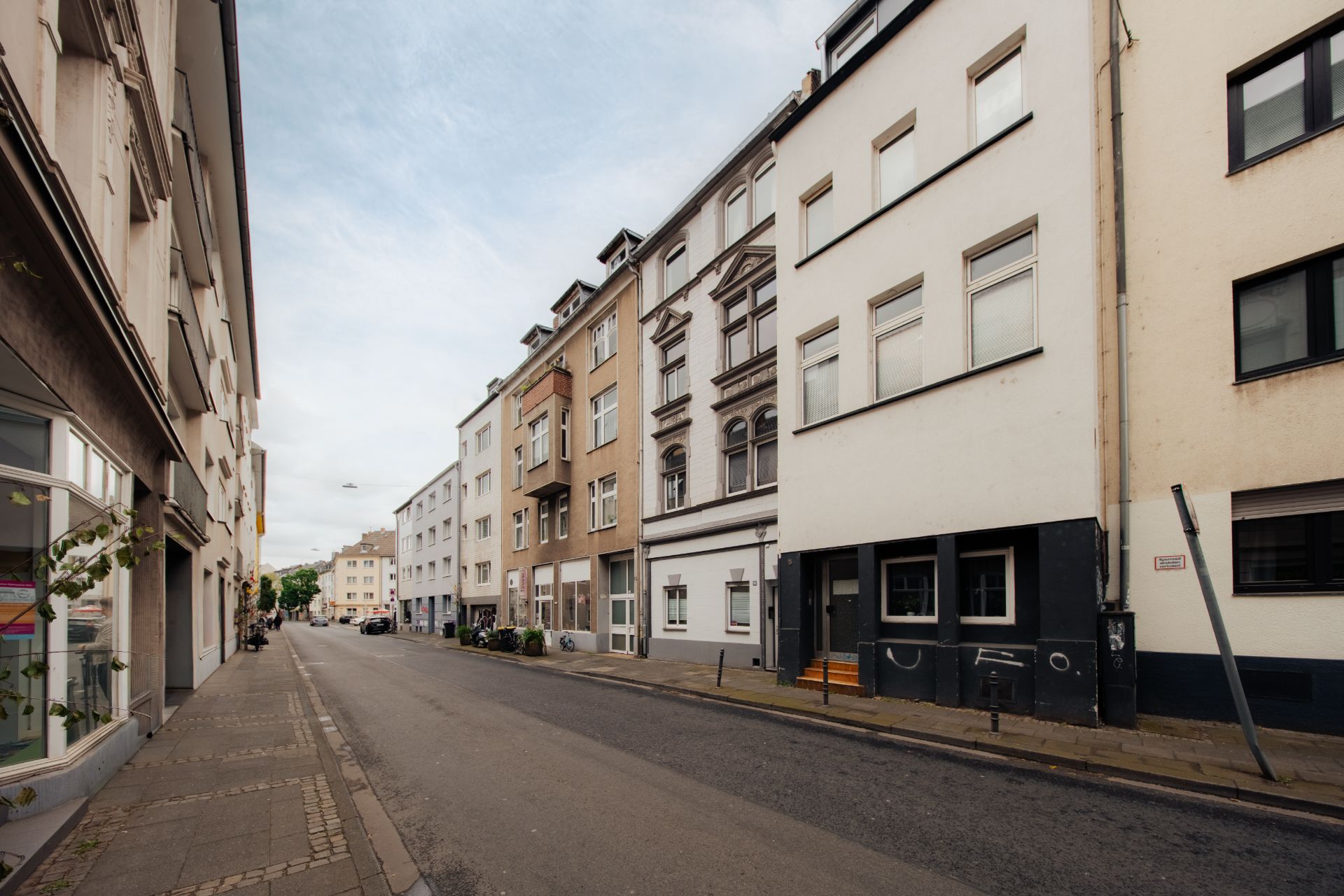 Schmale Wohnstraße mit mehrstöckigen Häusern und Gehweg bei Tageslicht.
