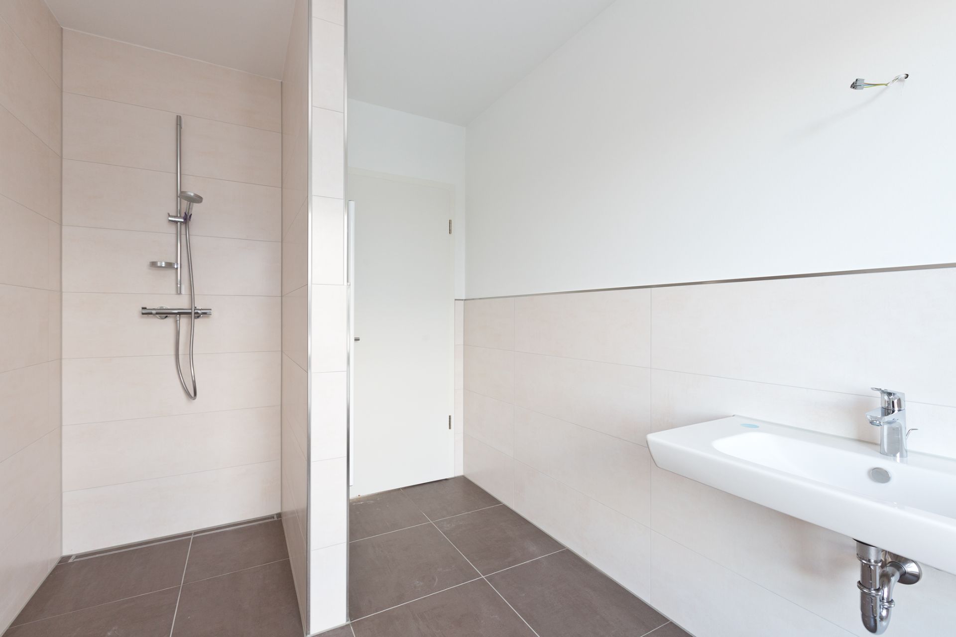 Modernes Badezimmer mit offener Dusche und weißem Waschbecken, helle Fliesen an Wand und Boden.