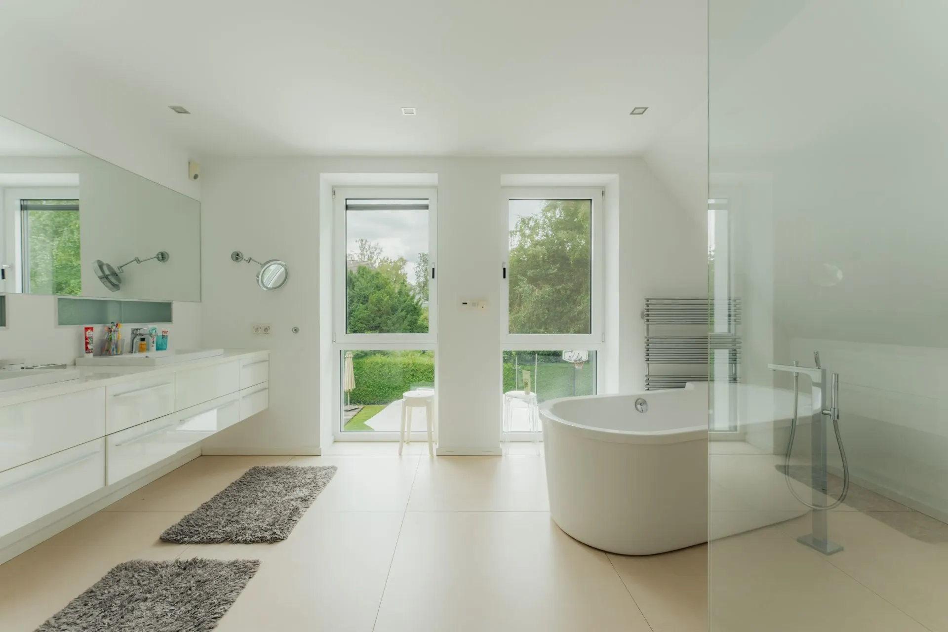 Modernes Badezimmer mit freistehender Badewanne, zwei Fenstern und langem Waschtisch mit Spiegel.