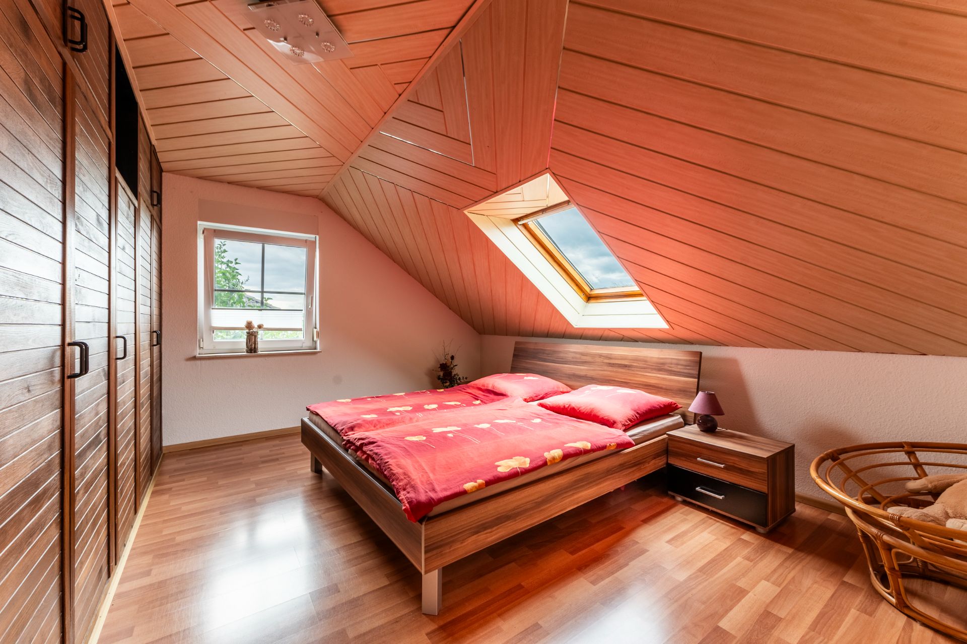 Dachgeschoss-Schlafzimmer mit Holzdecke, Doppelbett, Fenster und Nachttisch.