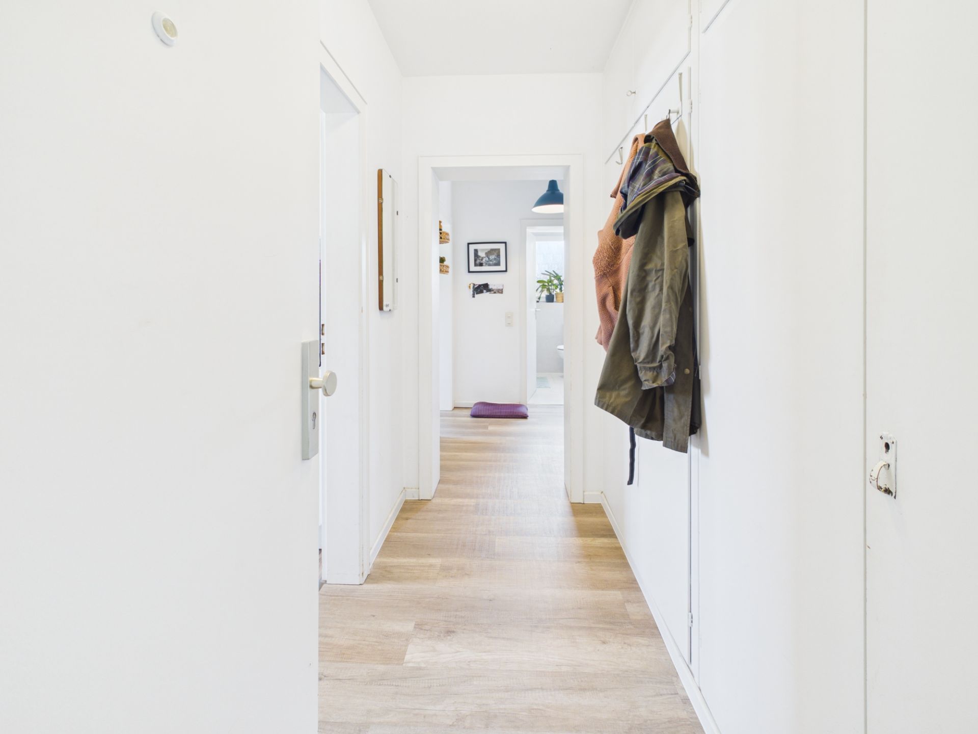 Heller Flur mit Holzboden, Garderobe und Jacken an der Wand.