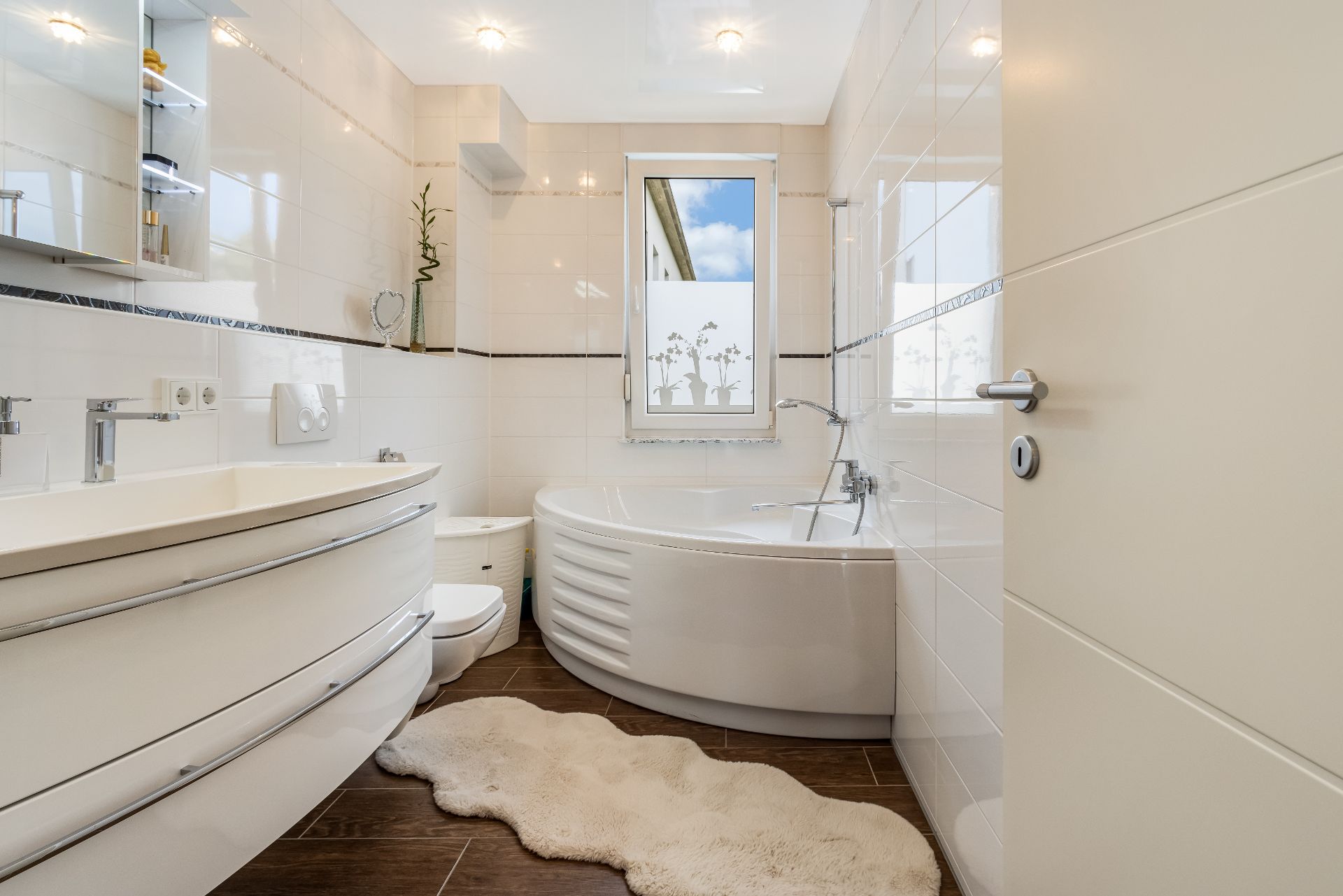 Modernes Bad mit Eckbadewanne, Doppelwaschbecken, Spiegel und Fenster, brauner Boden und weißer Teppich.