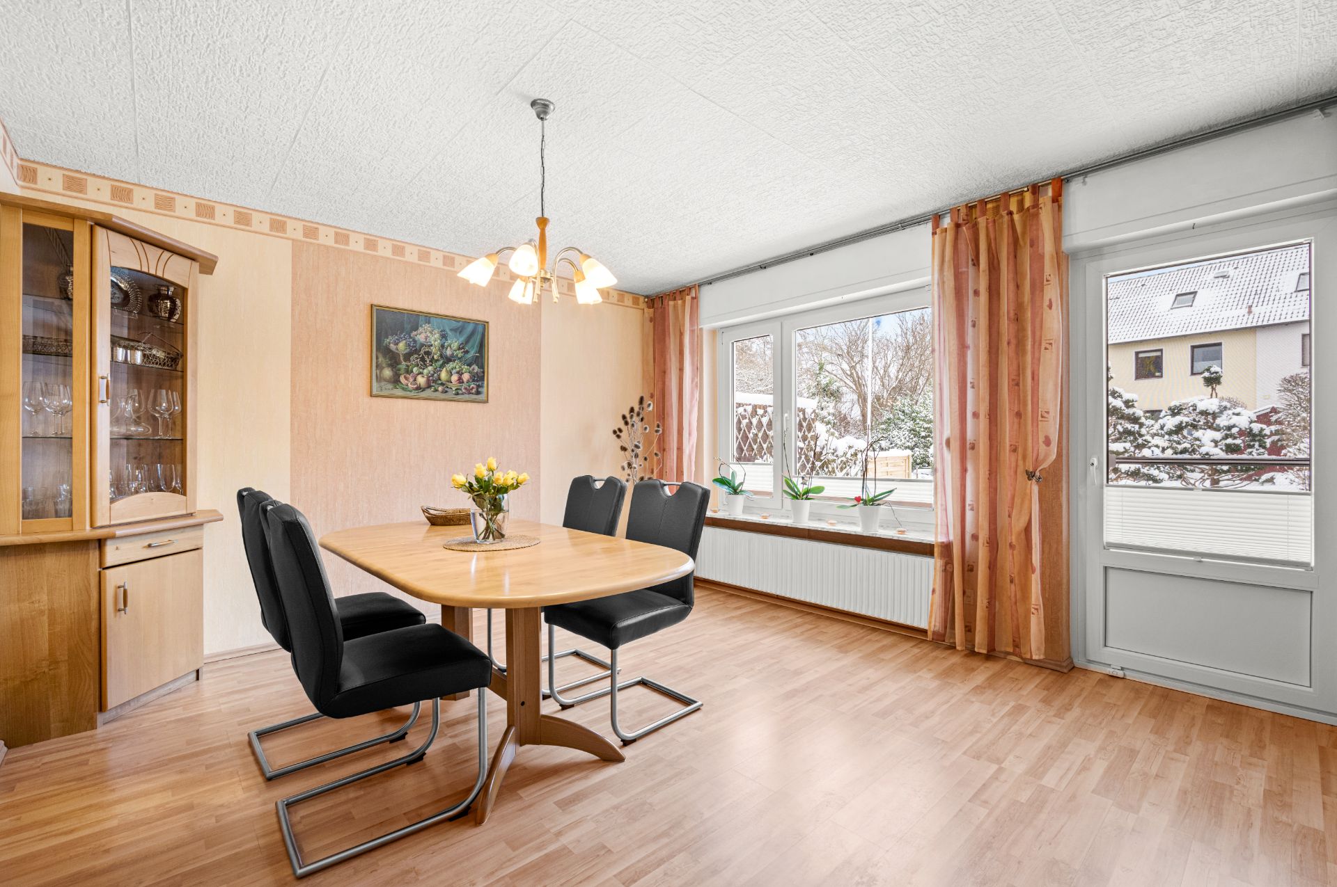 Helles Esszimmer mit Holztisch, sechs schwarzen Stühlen, Vitrine und großem Fenster mit Blick nach draußen.