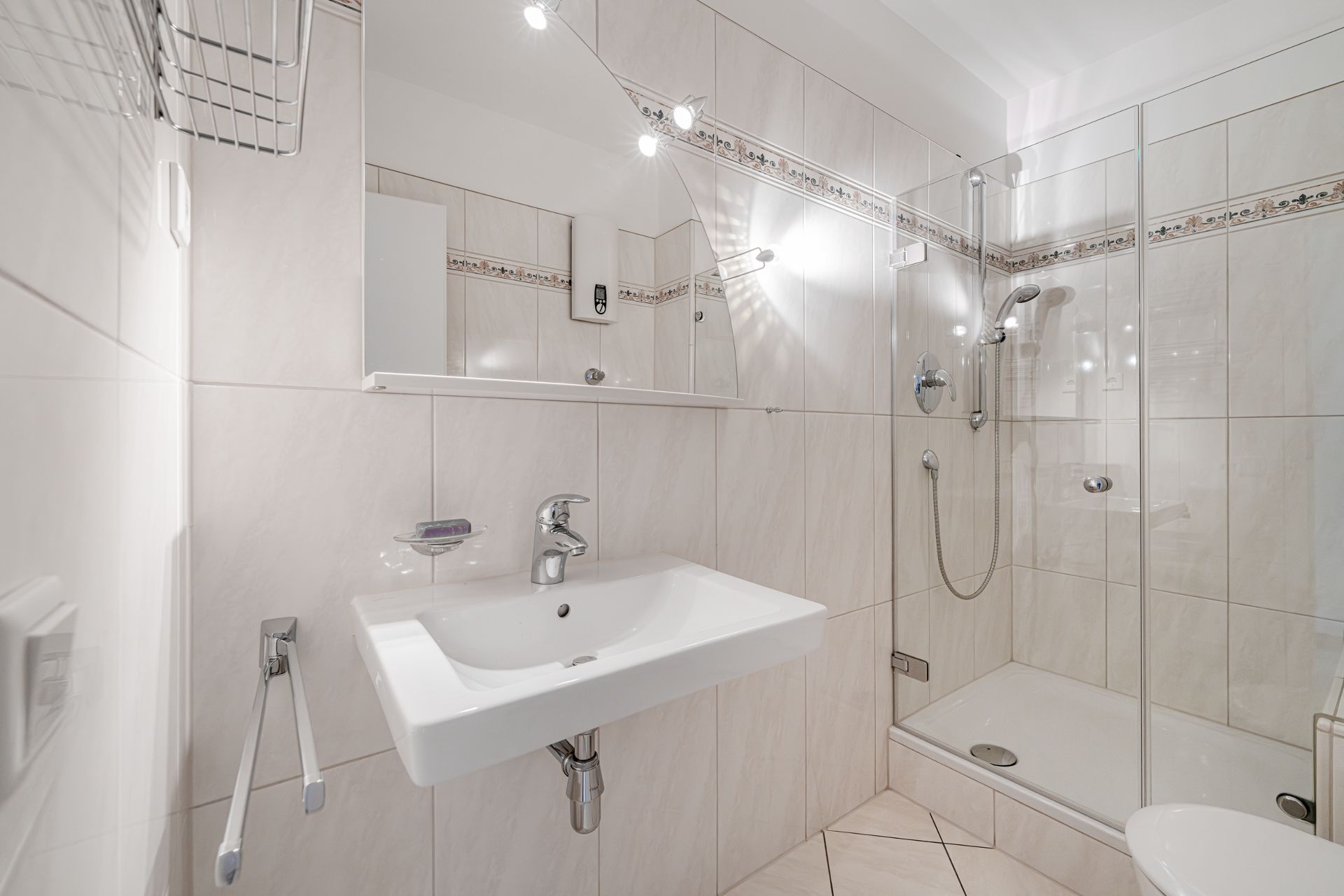 Helles Bad mit Waschbecken, Spiegel, Dusche mit Glastür und weißen Fliesen.