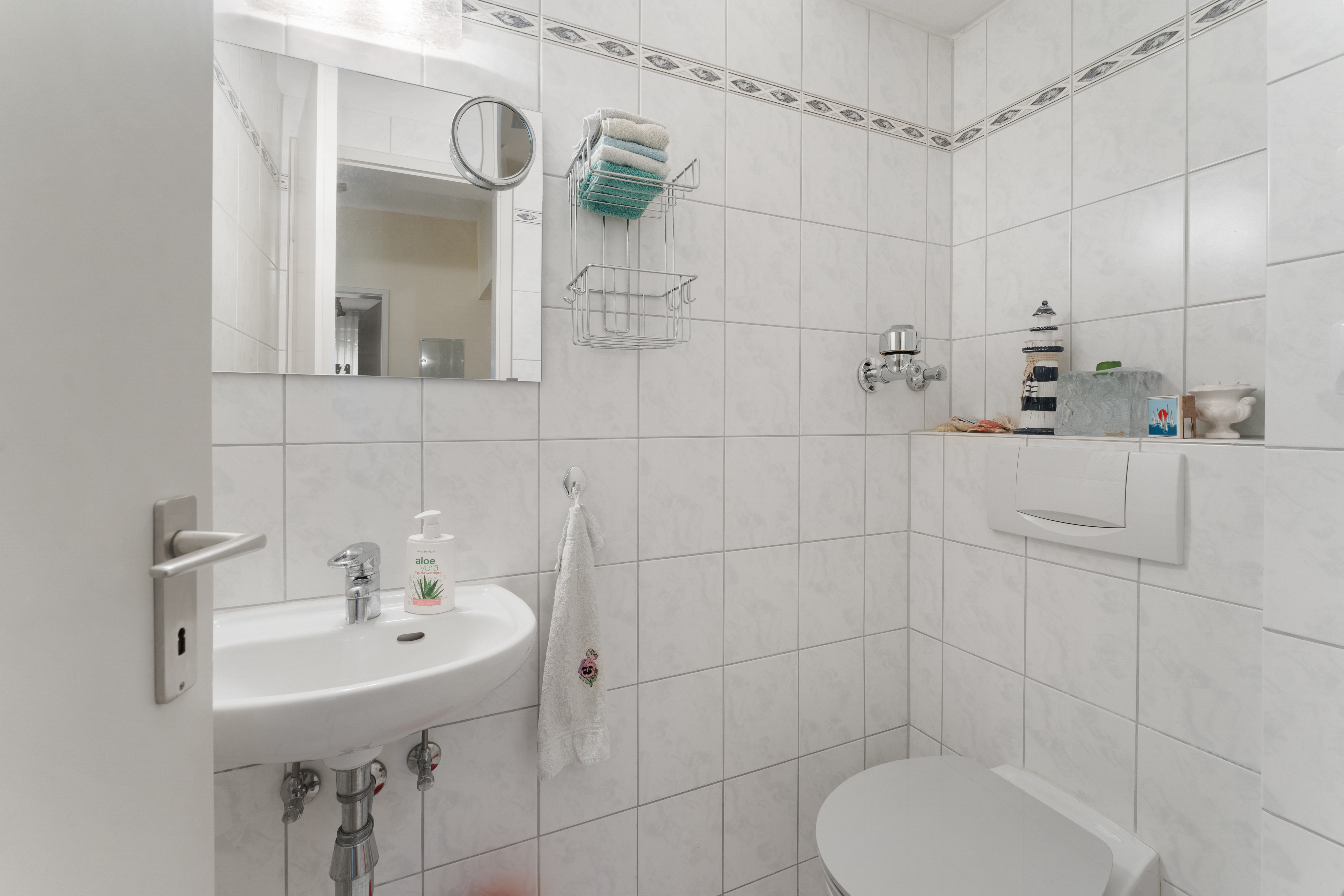Kleines Badezimmer mit weiß gefliesten Wänden, Waschbecken, Spiegel und Toilette.