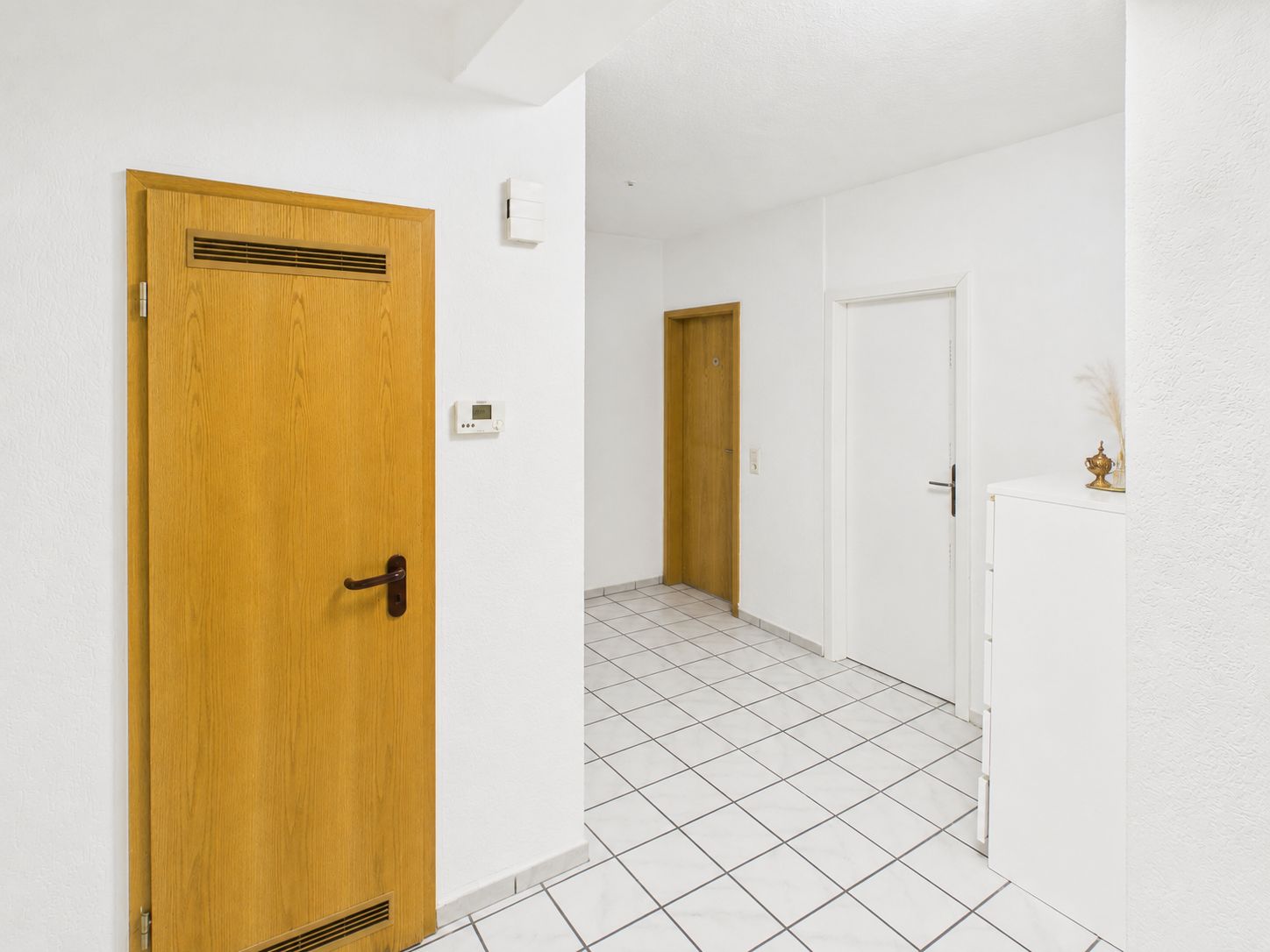 Heller Flur mit weißen Wänden, Fliesenboden und drei Türen, davon zwei aus Holz.