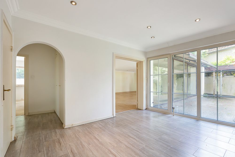 Heller Raum mit Fliesenboden, Glas-Schiebetüren und Zugang zu einem anderen Zimmer.