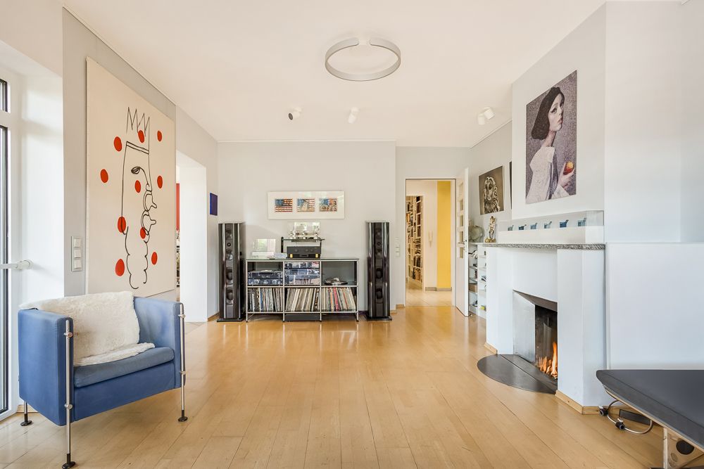 Modernes Wohnzimmer mit Holzboden, blauem Sessel, Kamin und Wandbildern.