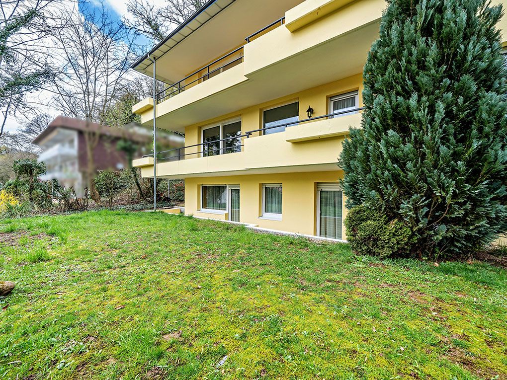 Gelbes Wohnhaus mit Balkonen und großer Wiese im Vordergrund, Baum rechts.