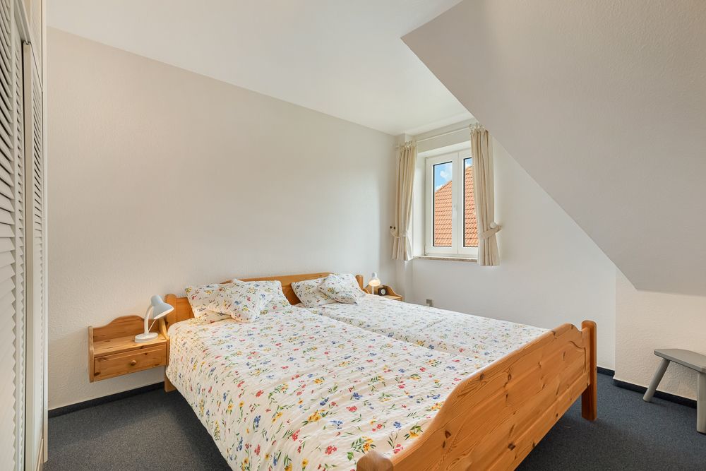 Helles Schlafzimmer mit zwei Einzelbetten, Blumenbettwäsche und Fenster mit Vorhängen.