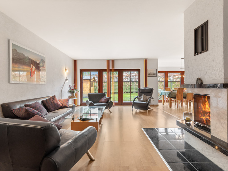 Helles Wohnzimmer mit Kamin, Sesseln, Sofa und großen Fenstern zum Garten.
