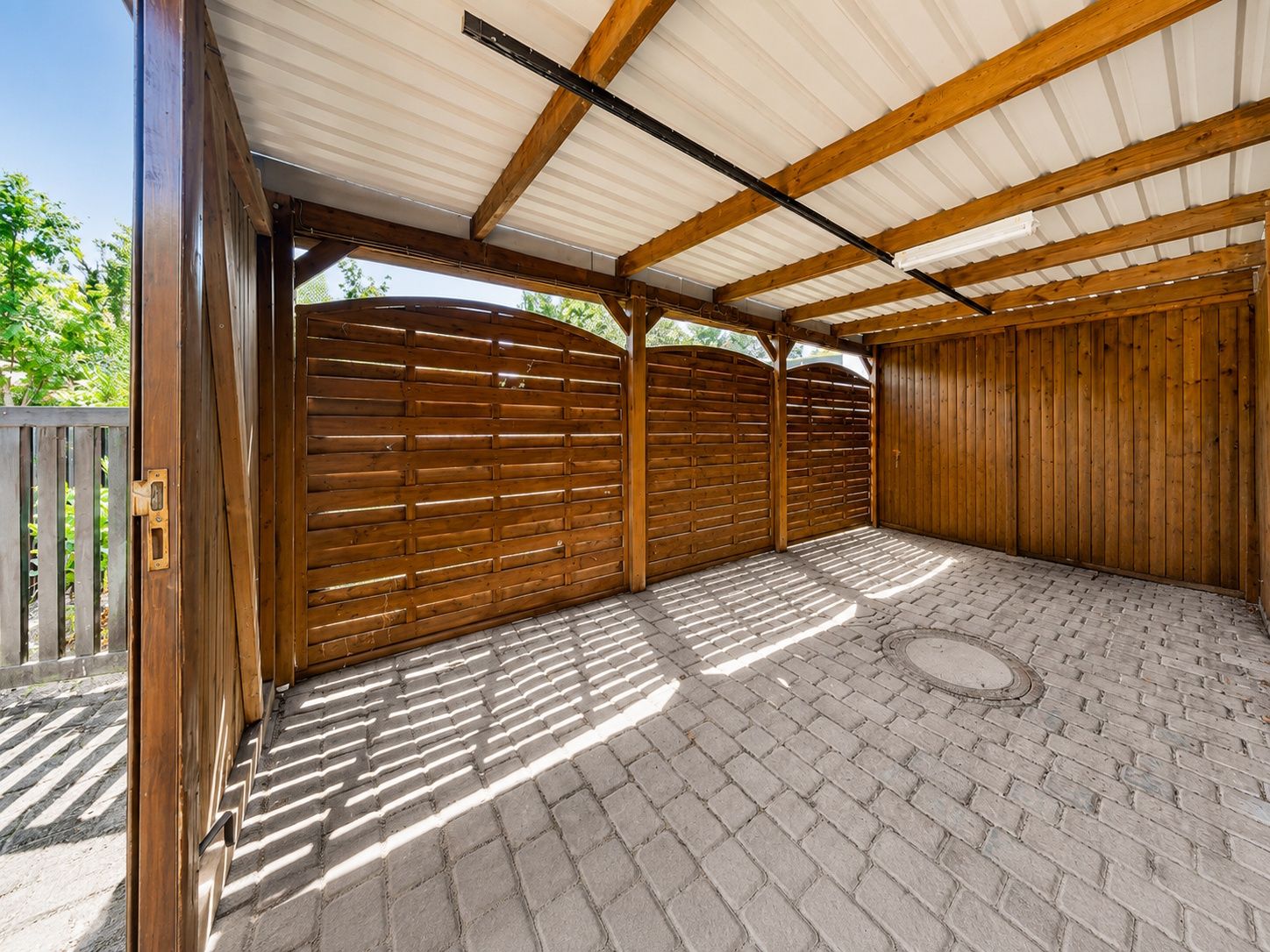 Überdachter Carport mit Holzwänden und Pflastersteinboden.