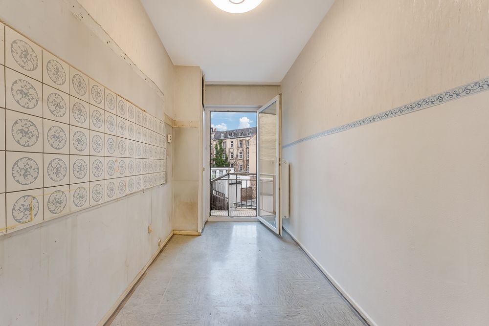 Leerer Raum mit Fliesen an der Wand und offener Tür zu einem Balkon mit Stadtblick.