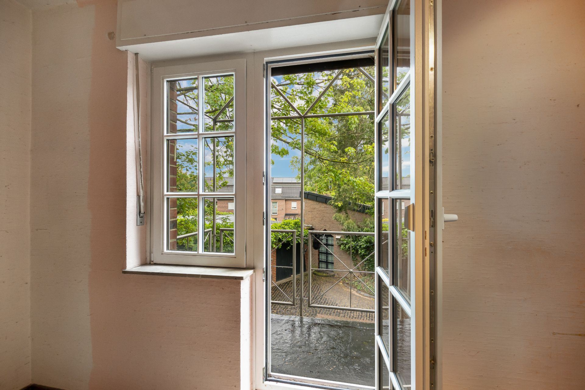 Geöffnetes Fenster mit Blick auf einen kleinen Balkon und grüne Bäume im Innenhof.