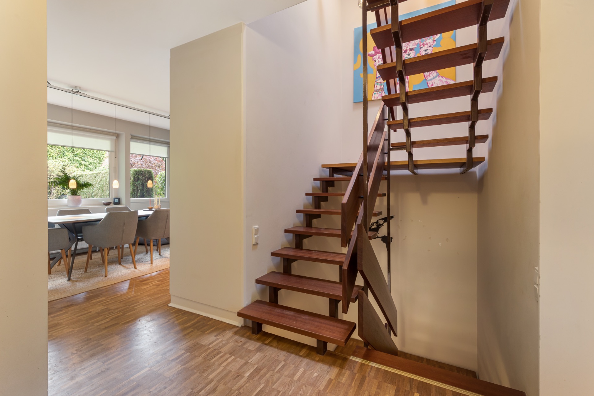 Holztreppe im Eingangsbereich mit Blick ins Esszimmer, große Fenster im Hintergrund.