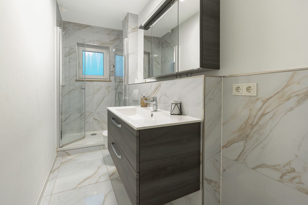 Modernes Badezimmer mit Dusche, Waschbecken, Spiegelschrank und Fliesen in Marmoroptik.