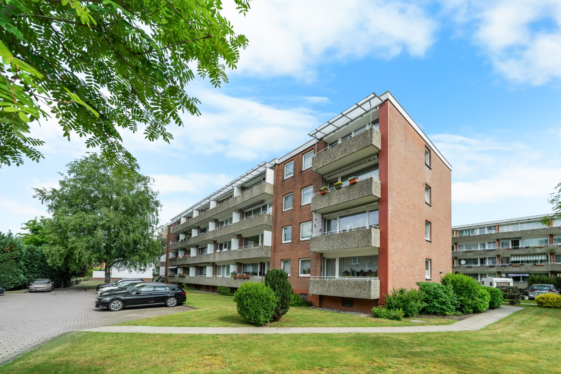 Mehrstöckiges Wohnhaus mit Balkonen und gepflegtem Vorgarten an einem sonnigen Tag.