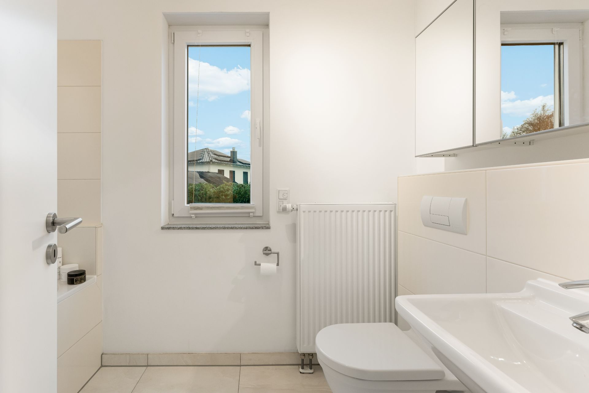 Modernes, helles Bad mit Fenster, Waschbecken, WC, Heizung und Spiegel.