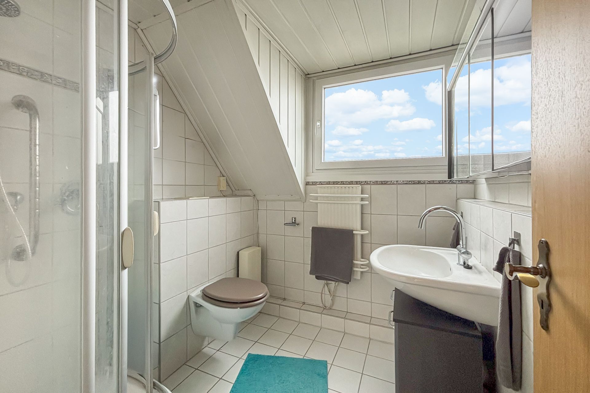 Helles Badezimmer mit Dusche, WC, Waschbecken, Handtuchheizkörper und Fenster.