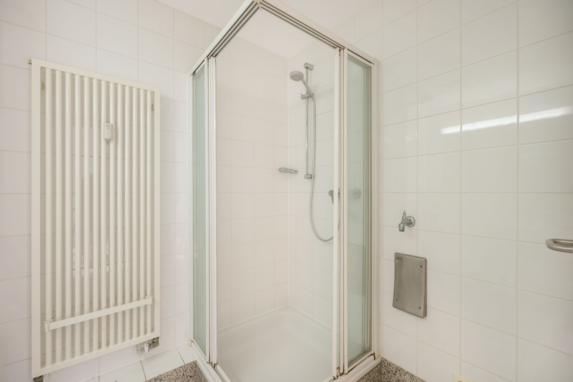 Helles Badezimmer mit Dusche mit Glastüren und einem weißen Handtuchheizkörper an der Wand.