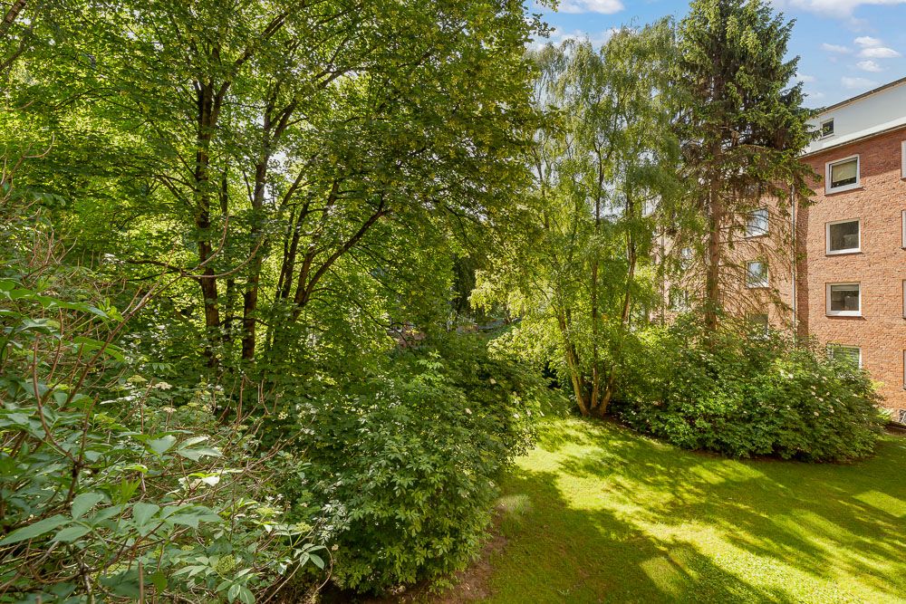 Grüner Garten mit Rasen, Bäumen und Sträuchern neben einem Wohngebäude.