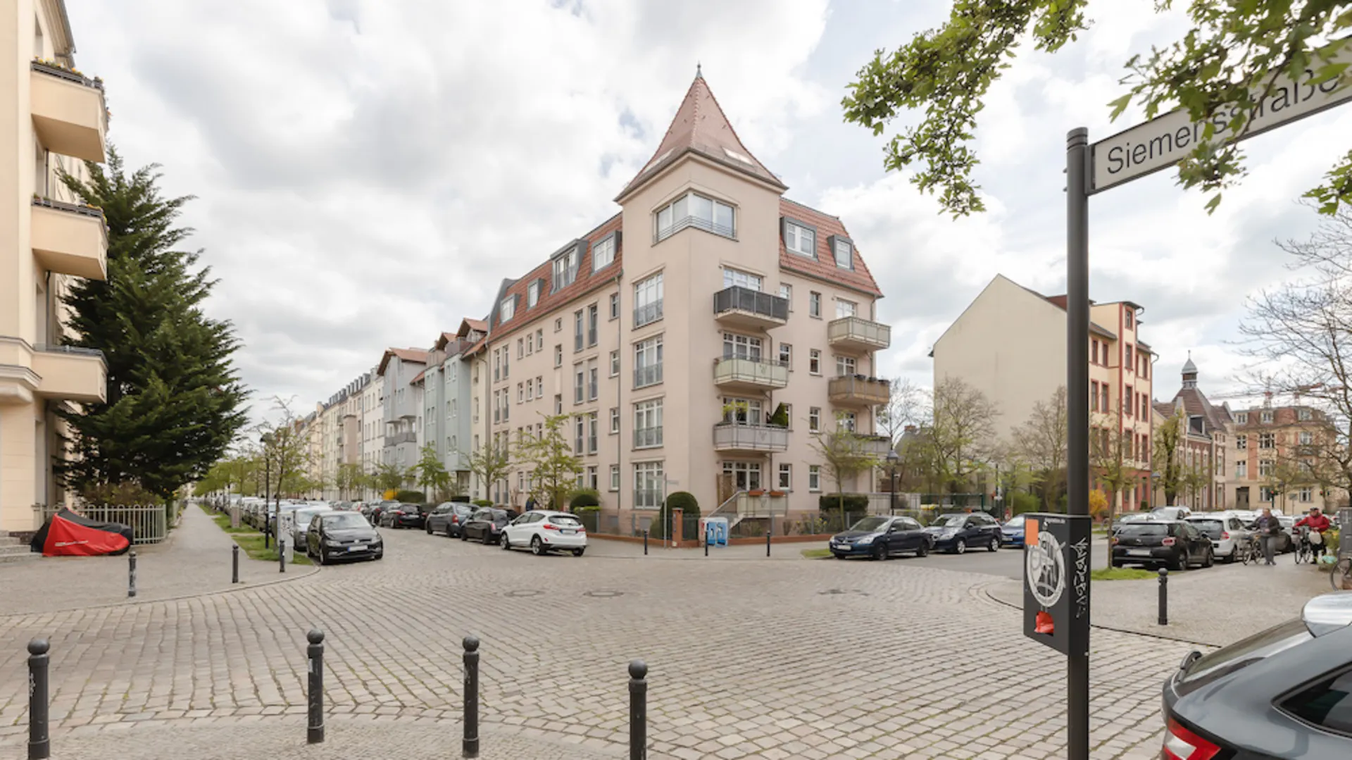 Straßenszene mit mehrstöckigen Wohnhäusern, parkenden Autos und Straßenschild Siemensstraße.